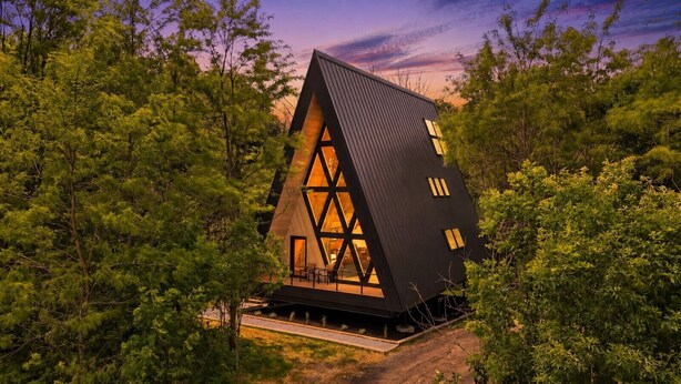 Une maison moderne, de forme triangulaire, entourée d’une forêt dense.