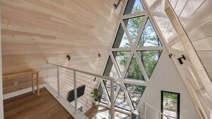 Un intérieur moderne avec des murs recouverts de panneaux de bois, un escalier doté de rampes en verre et une vue sur l’extérieur.