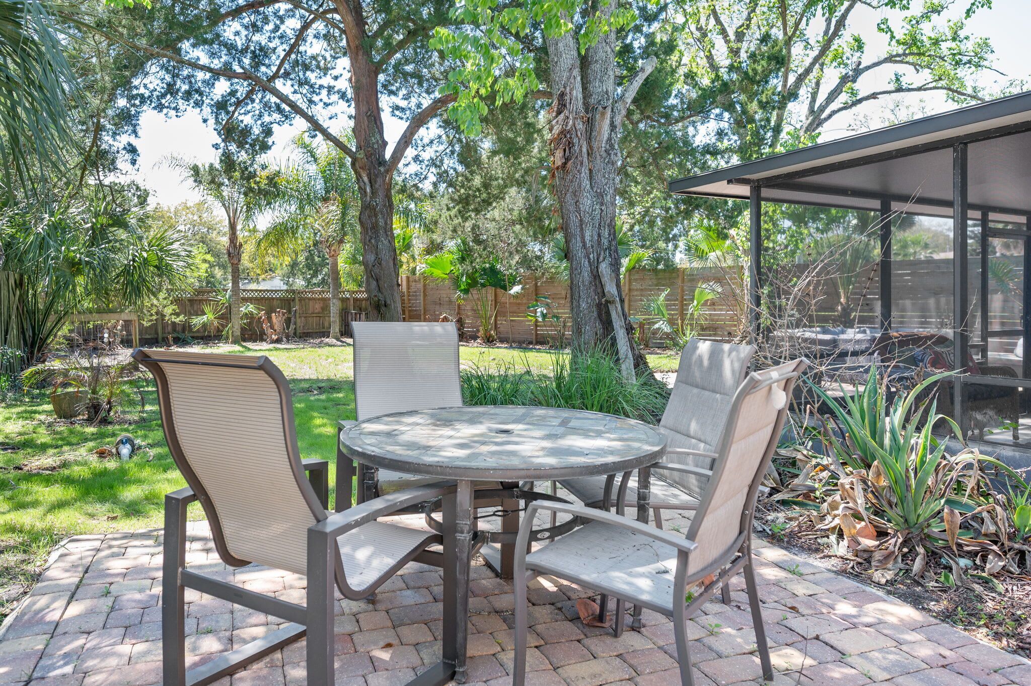 An outdoor patio with a round table and four chairs, surrounded by greenery and trees.