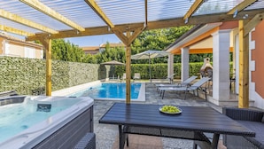 Ein überdachter Poolbereich mit Whirlpool, Liegestühlen und einem Tisch mit Obstschale.