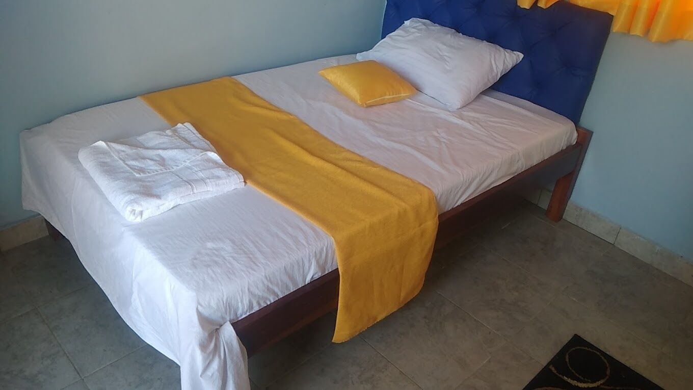 A neatly made bed with white and yellow linens, a blue headboard, and a small rug on the floor.