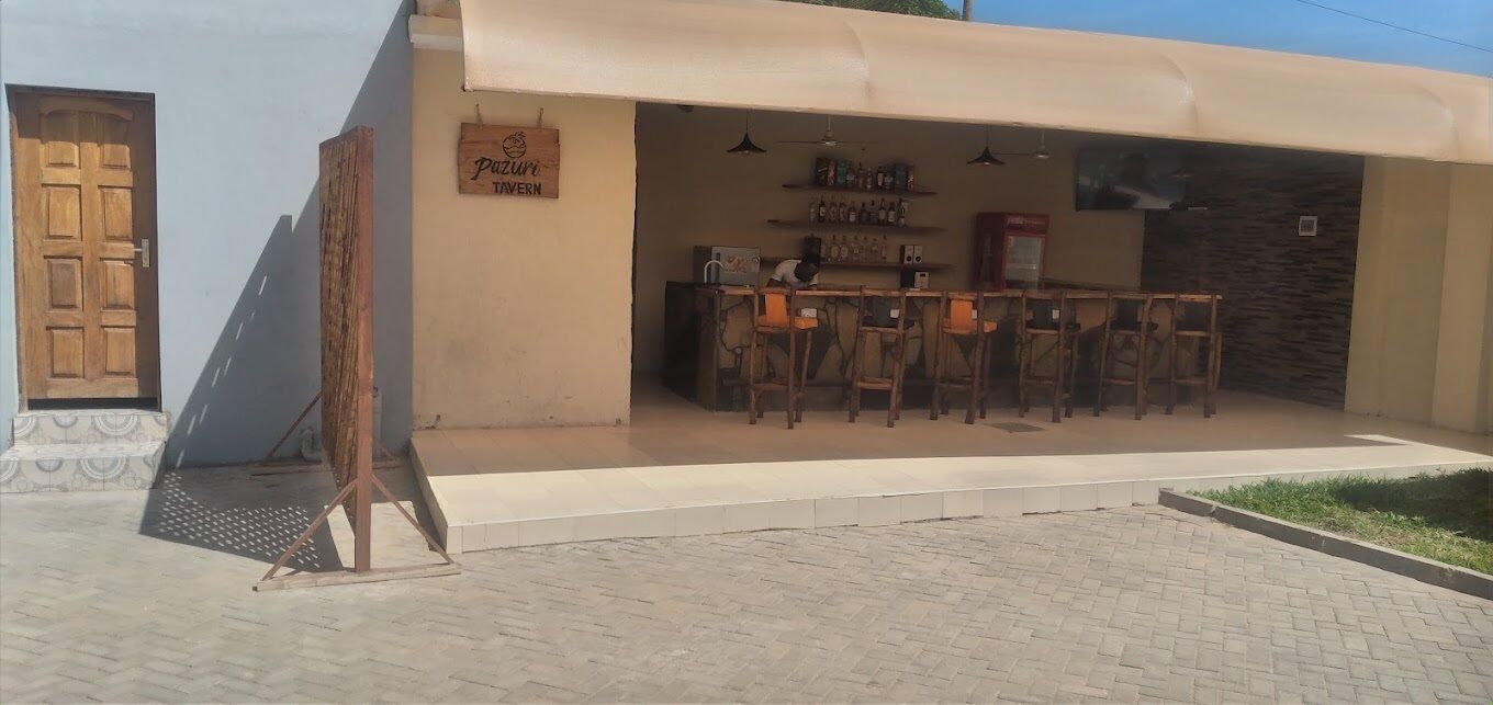 A bar area with wooden chairs and a counter, a sign reading "Pazuri Tavern," and a door to the left.
