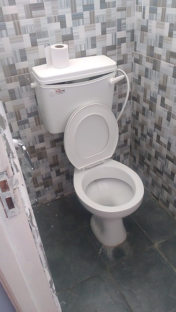 A bathroom with a toilet, a roll of toilet paper, and tiled walls.