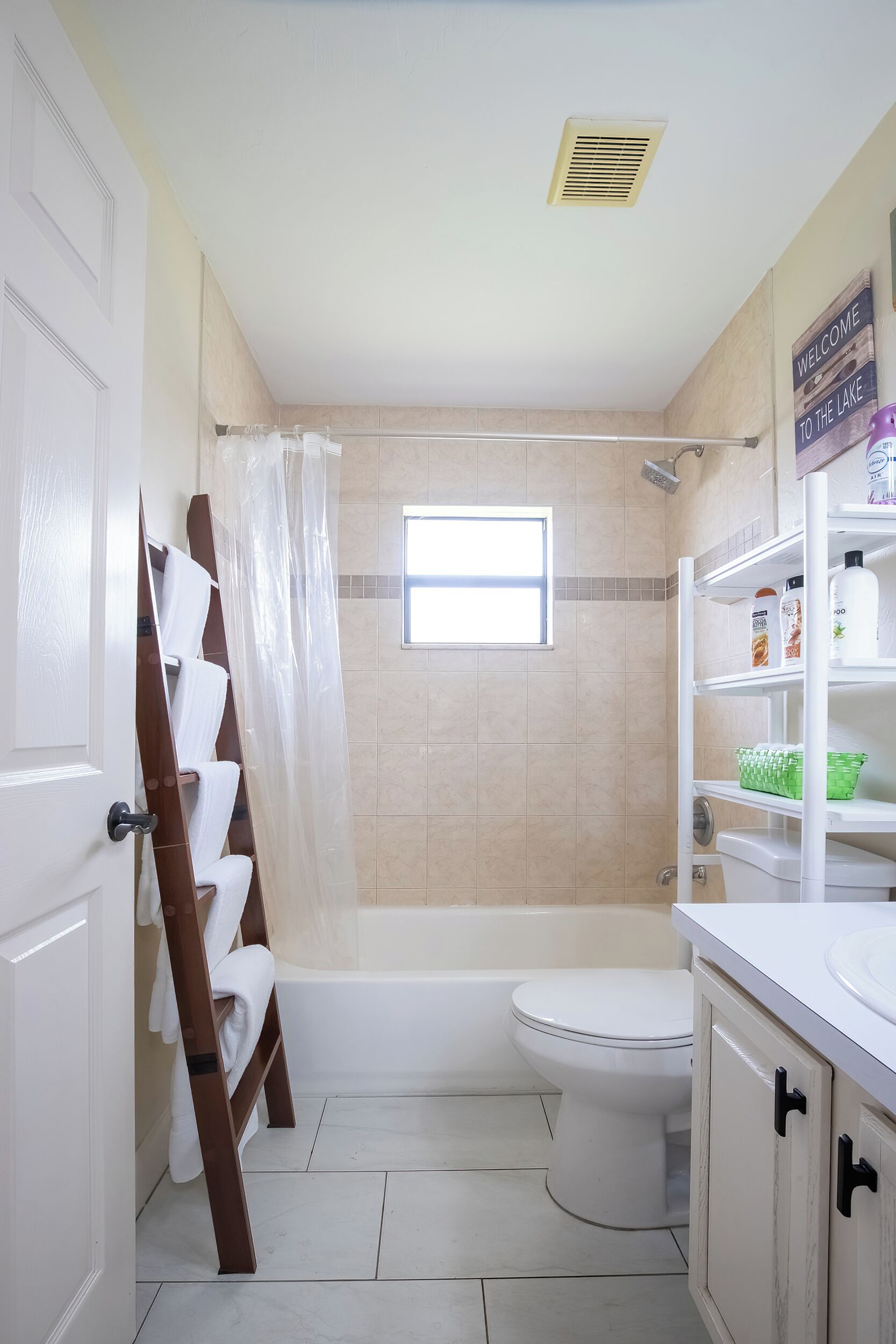 Ein Badezimmer mit einer Badewanne, Toilette und einer Duschvorhang. Ein Fenster sorgt für natürliches Licht, und ein Ablagefach bietet Platz für Pflegeprodukte.