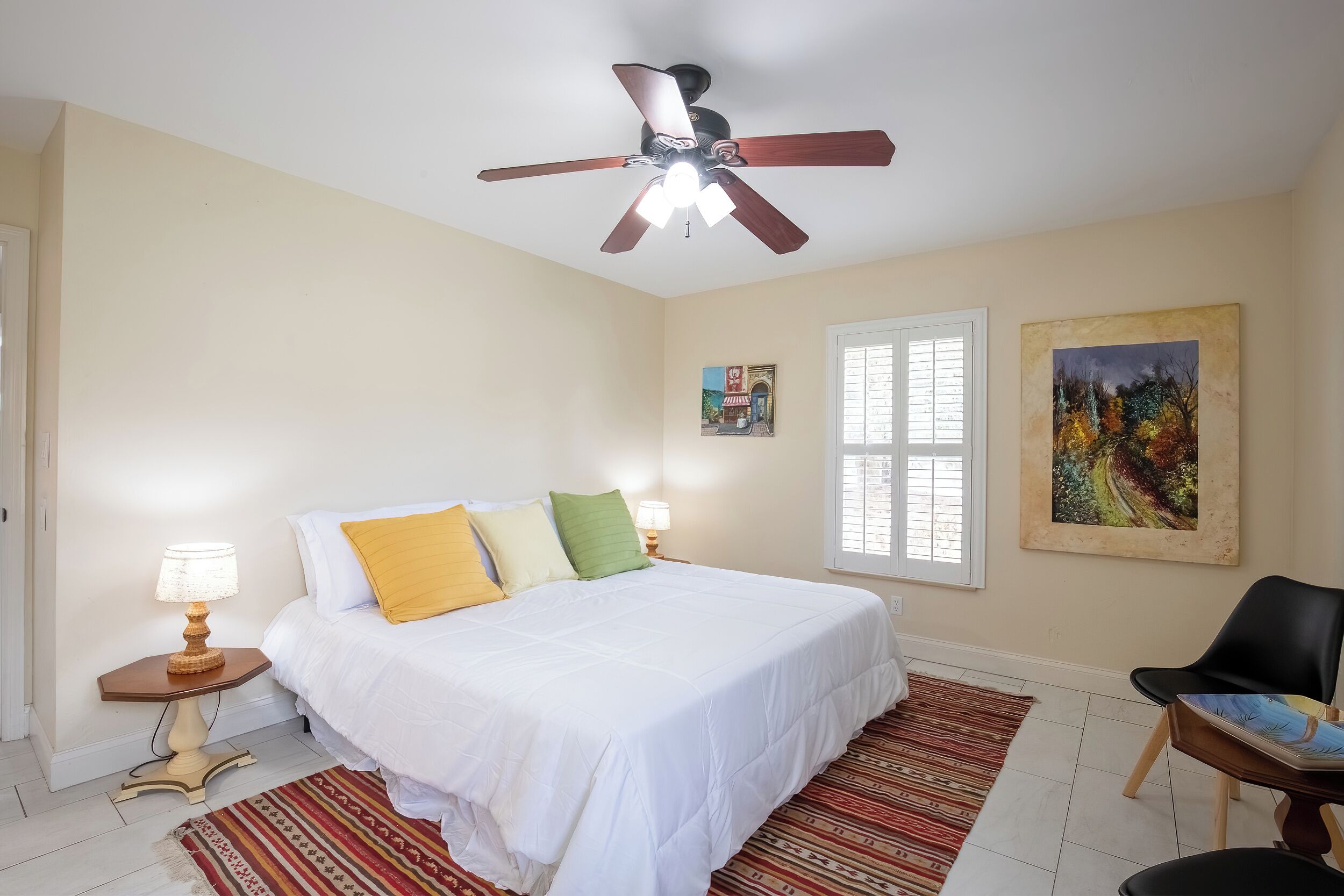 A bedroom with a bed, a ceiling fan, a window, and a chair.