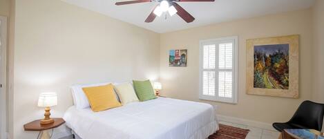 A bedroom with a bed, a ceiling fan, a window, and a chair.