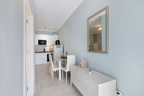 A compact kitchen with white cabinetry, a dining table with chairs, a small potted plant, and a mirror on the wall. - Apartment 'Sun7set' near the beach with Wi-Fi and air conditioning (Quarteira)