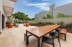 An outdoor patio with a wooden table and chairs, surrounded by planters and seating. - Brooklyn • Emma's bed • 7 min subway • Berrini (São Paulo)