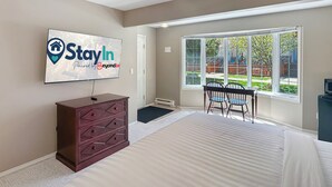 Un dormitorio con cama, cómoda, televisor montado en la pared, ventana y puerta.