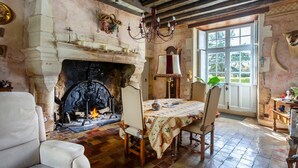 A room with a fireplace, a dining table with chairs, a chandelier, and a large window. - Castle 'Chambre 1' with Shared Terrace, Private Garden and Wi-Fi (La Boixe)