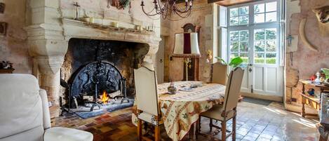 A room with a fireplace, a dining table with chairs, a chandelier, and a large window.