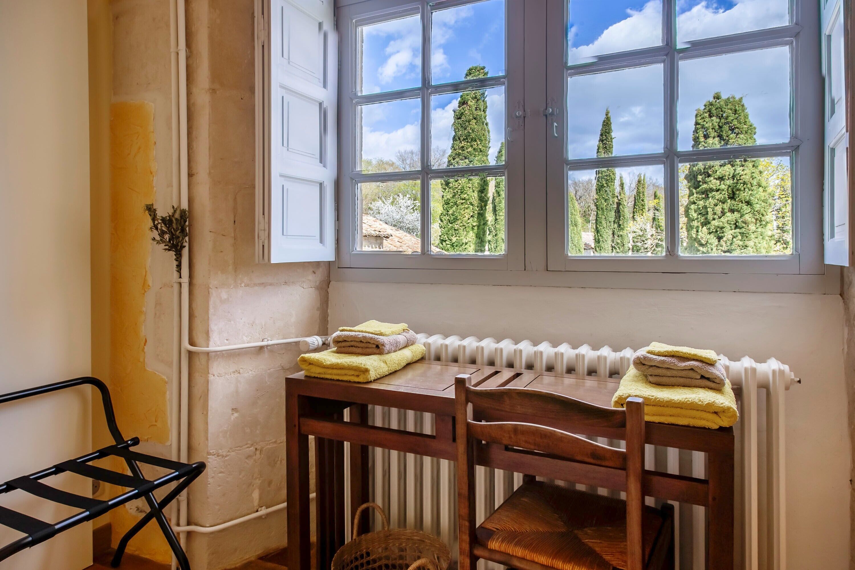 Una habitación con ventana, radiador, una mesa de madera, sillas y una silla de metal negro.