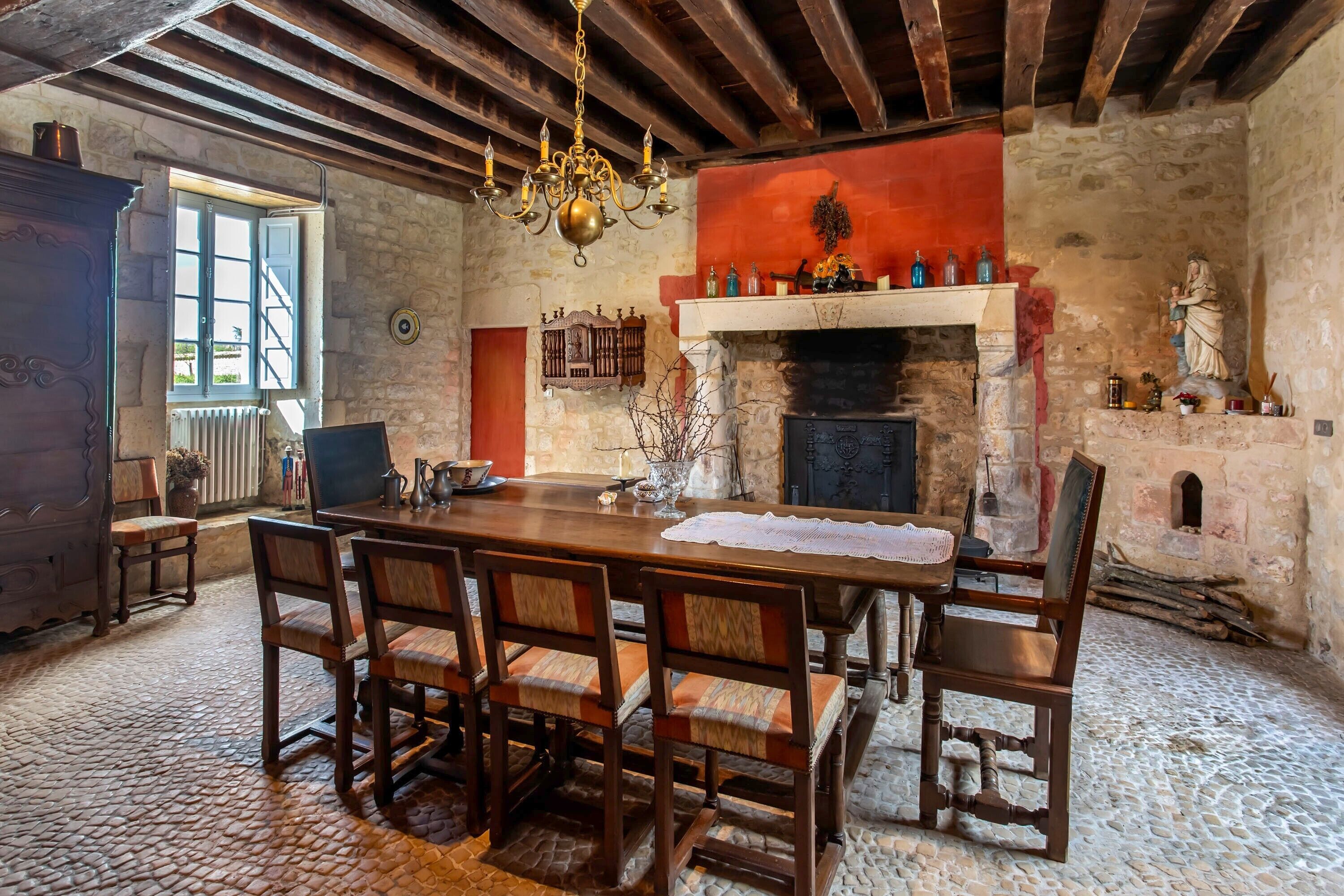 A rustic dining area with a stone fireplace, wooden furniture, and a chandelier.