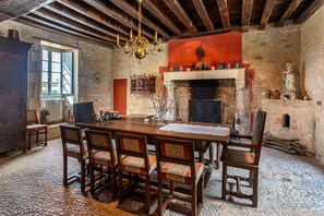 Uma sala de jantar rústica com lareira de pedra, mobiliário de madeira e um candelabro.