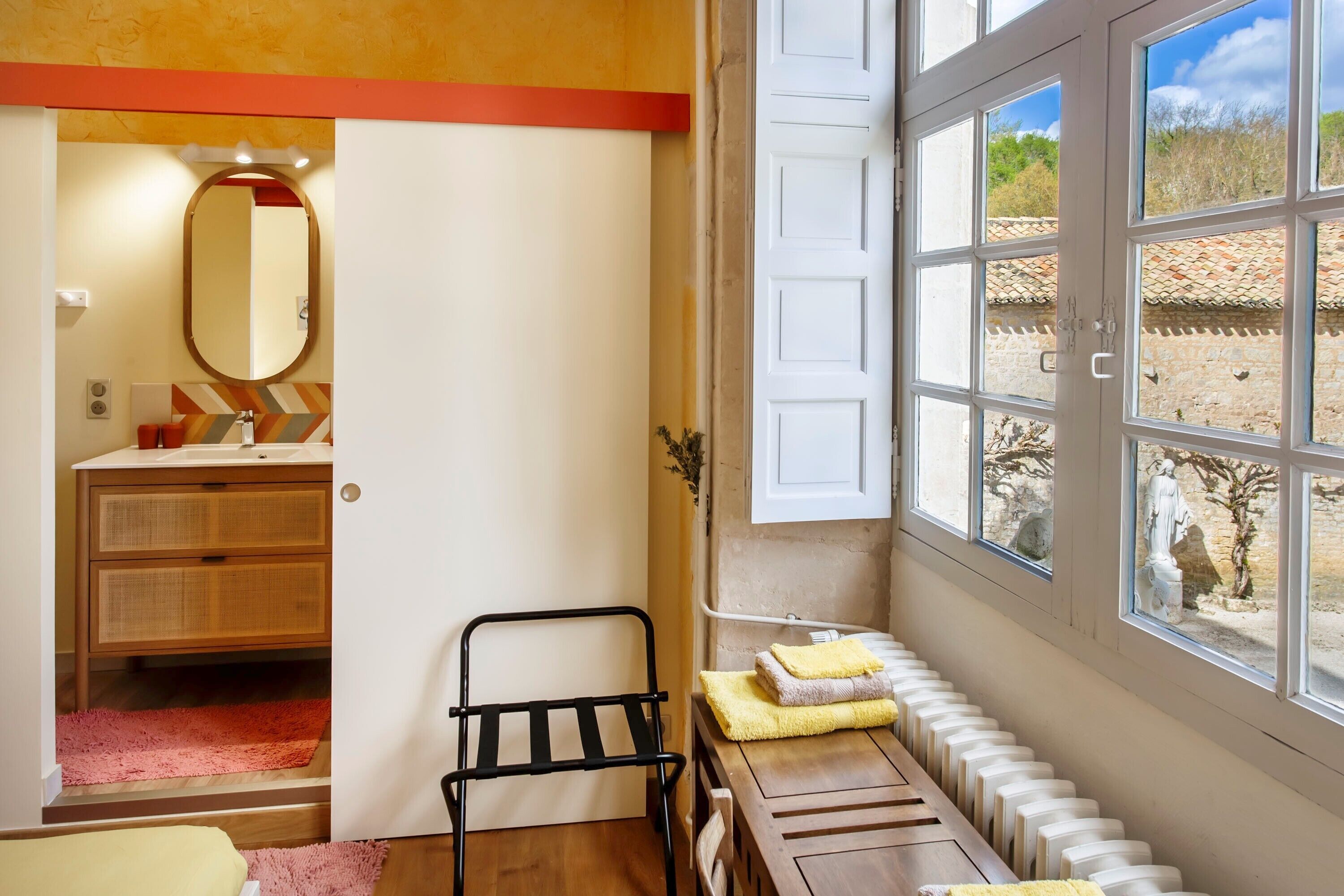 A room with a wooden bench, a mirror, a window with a view of the outside, and a radiator.