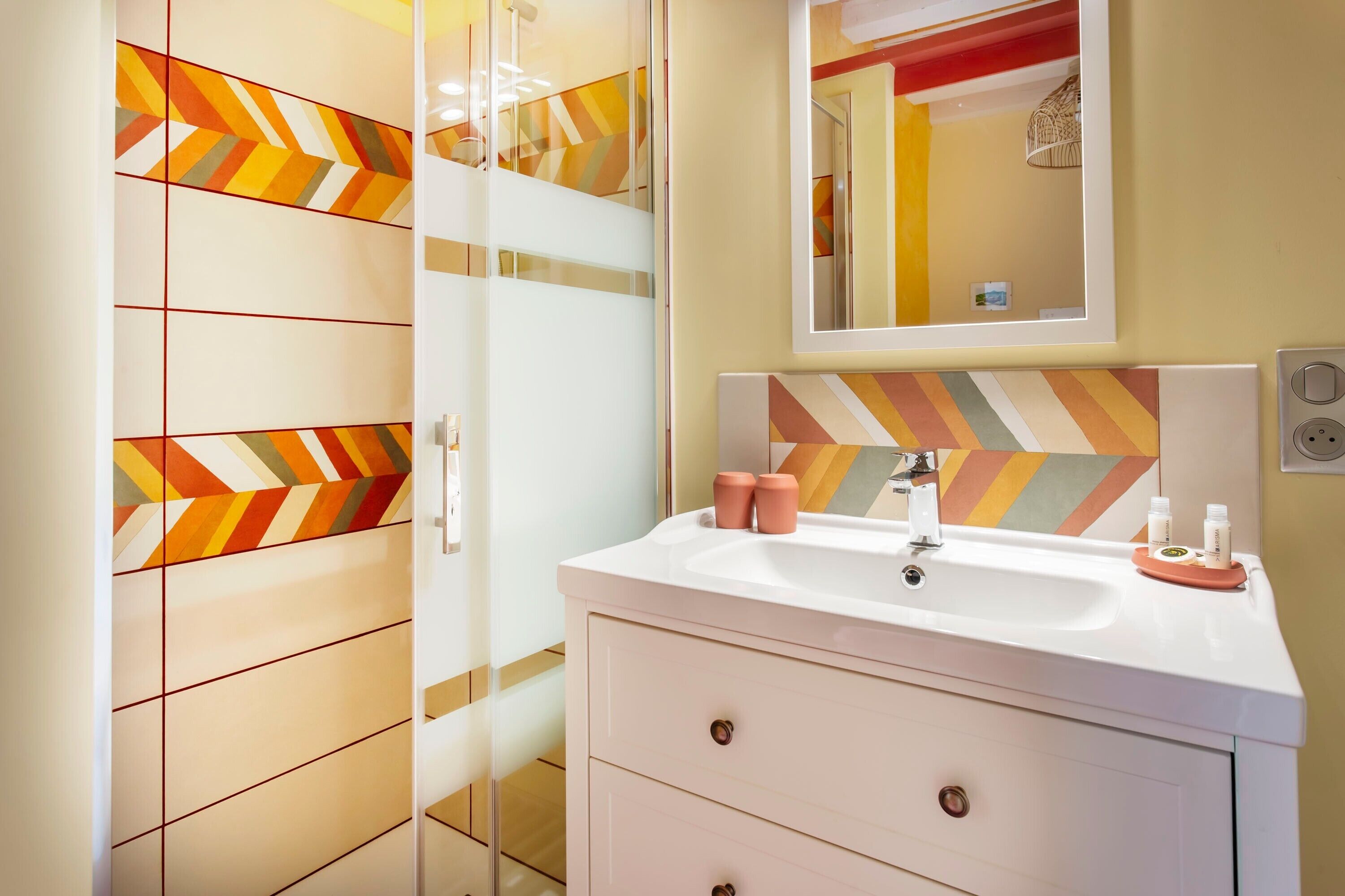A bathroom with a white sink, a mirror, and a geometric patterned wall.
