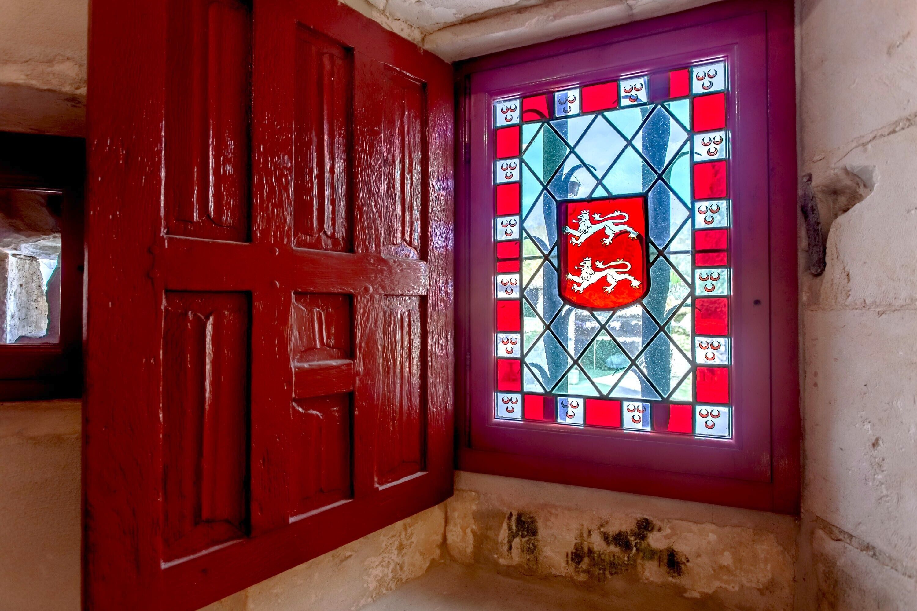 Une porte rouge ornée d’un vitrail représentant des armoiries.
