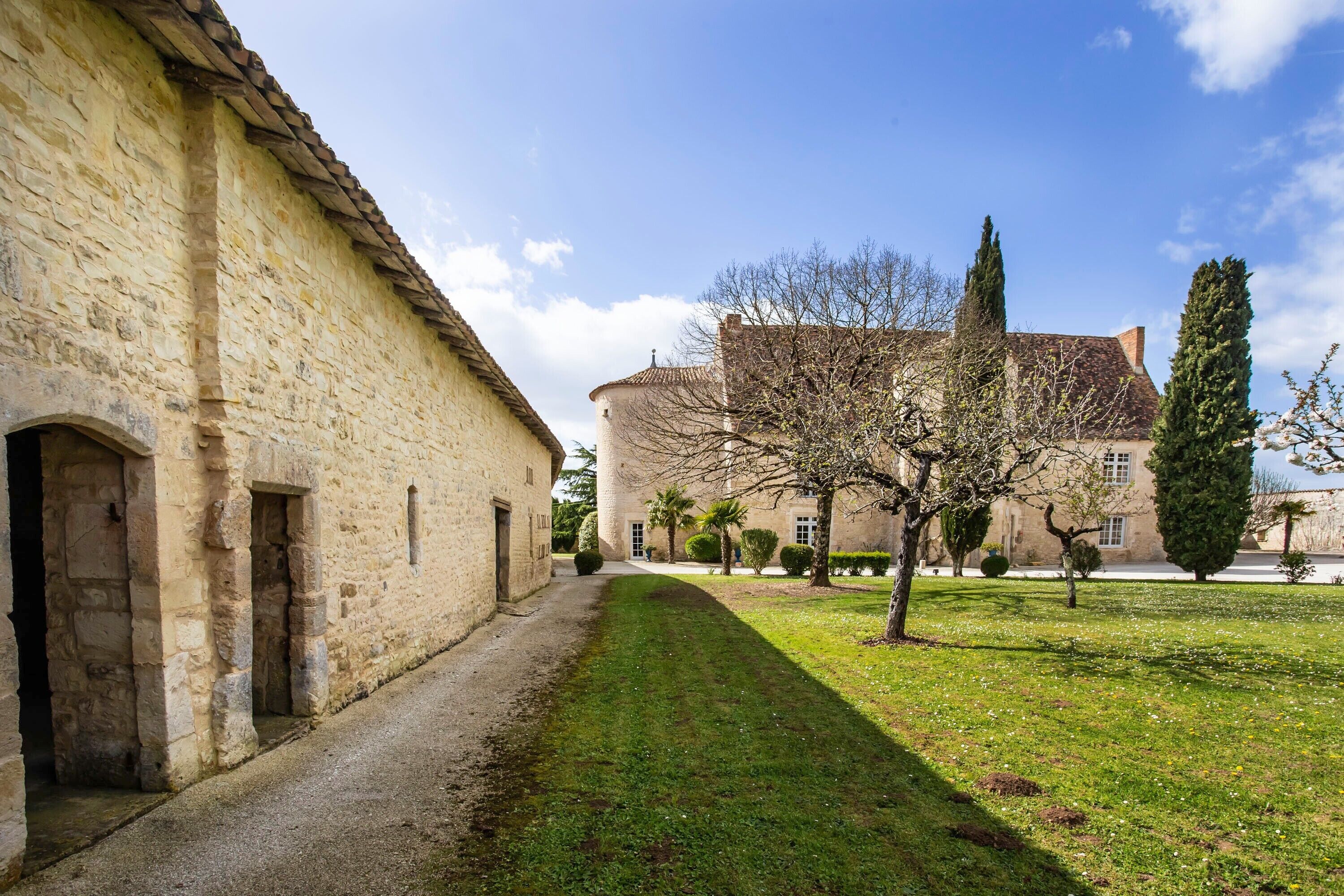 Un bâtiment en pierre doté d’une cour, d’une tour et d’un chemin bordé d’arbres.