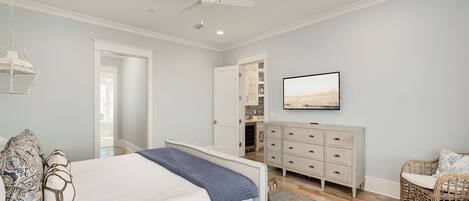 A bedroom with a bed, a dresser, a television, and a ceiling fan.