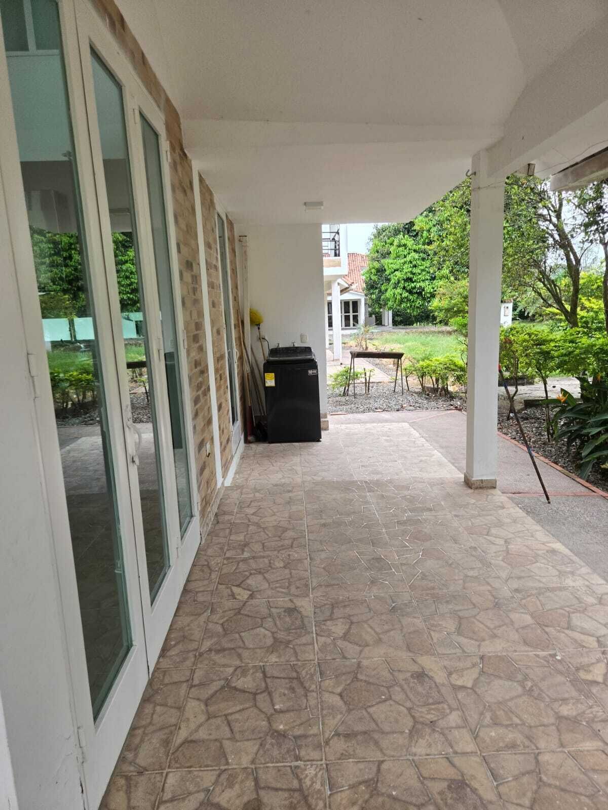 A covered outdoor area with stone flooring, large glass doors, and a view of a garden and buildings in the background.