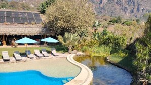 A swimming pool with lounge chairs and umbrellas, surrounded by greenery and mountains in the background. - Bambu Villas Wellness Center (Amatlán)