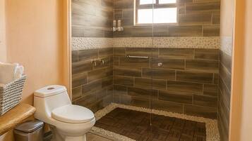 Een badkamer met douche, toilet en een raam.