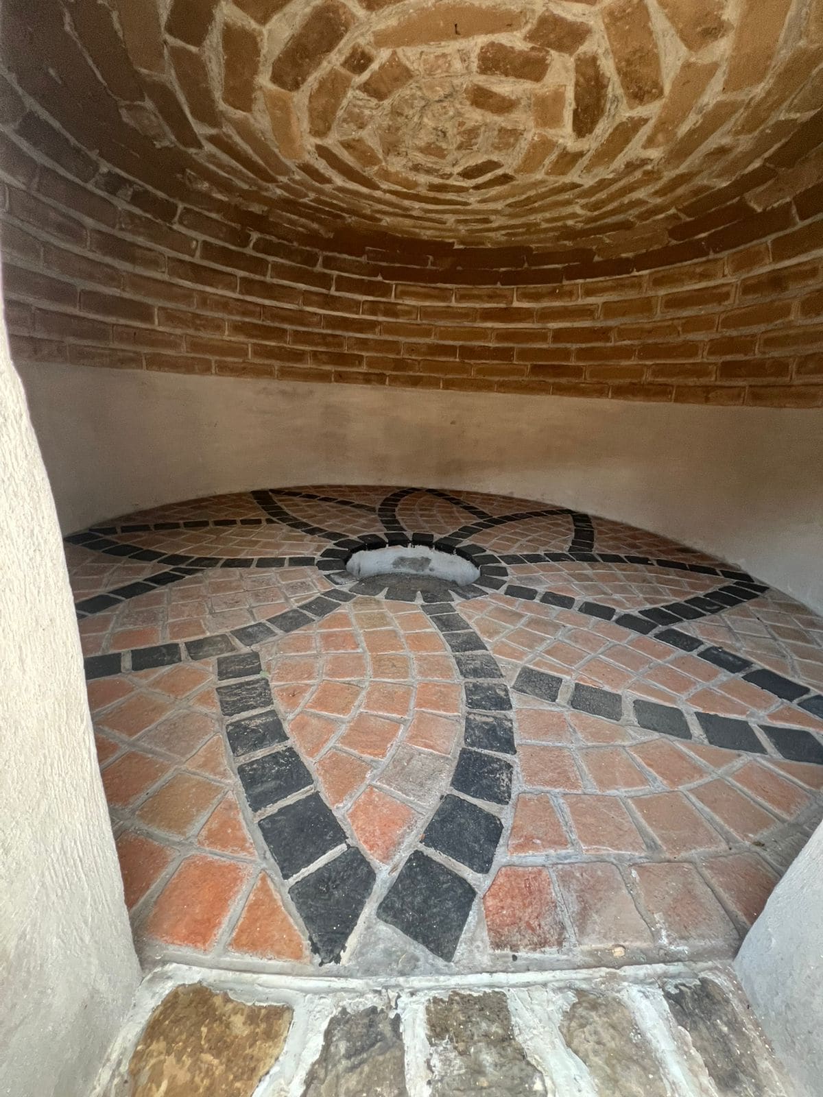 A circular stone-tiled floor with a brick wall and a white pillar.
