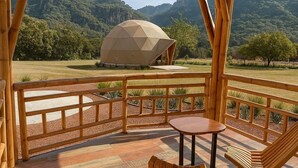 A wooden deck with a table and chairs, overlooking a mountainous landscape and a geodesic dome structure. - Bambu Villas Wellness Center (Amatlán)