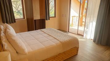 A bedroom with a bed, wooden flooring, a wooden ceiling, a window, and a door leading to an outdoor area.