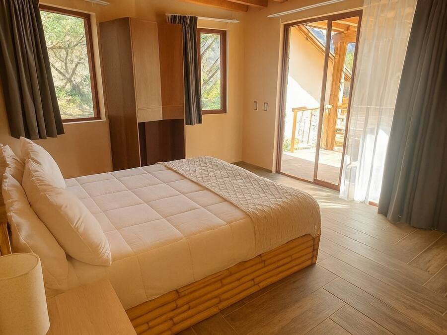 A bedroom with a bed, wooden flooring, a wooden ceiling, a window, and a door leading to an outdoor area.
