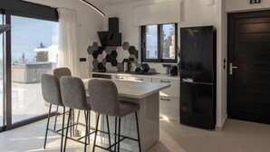 Eine moderne Küche mit einer zentralen Kochinsel, Barhocker, einem schwarzen Kühlschrank und Blick ins Freie.