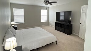 Ein Schlafzimmer mit einem Bett, einem Deckenventilator, einem Fernseher und einem Nachttisch mit einer Lampe.