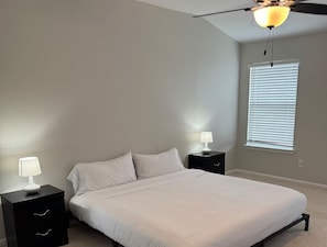 Un dormitorio con una cama, dos mesitas de noche, un ventilador de techo y una ventana con persianas.