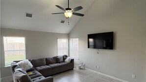 Ein Wohnzimmer mit einem grauen Ecksofa, einem Deckenventilator und einem flachbildfernseher, der an der Wand befestigt ist.