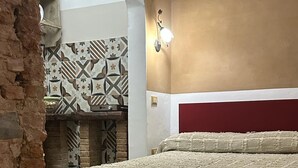 Une chambre avec un sol à motifs, un lit recouvert d’une couverture texturée, un mur orné de carreaux aux motifs géométriques et un mur en briques.