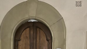 Une porte à deux battants en bois, avec une plaque métallique et un code QR apposé sur le mur à côté.
