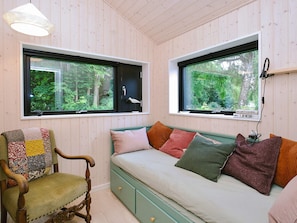 A room with a wooden paneled ceiling, a green sofa with multiple cushions, a wooden chair with a patchwork cushion, and two windows with views of greenery. - 4 Star Holiday Home in Gilleleje (Gilleleje)