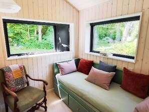 Un cuarto acogedor con un sofá verde, una silla de madera y dos ventanas con vistas a la vegetación.