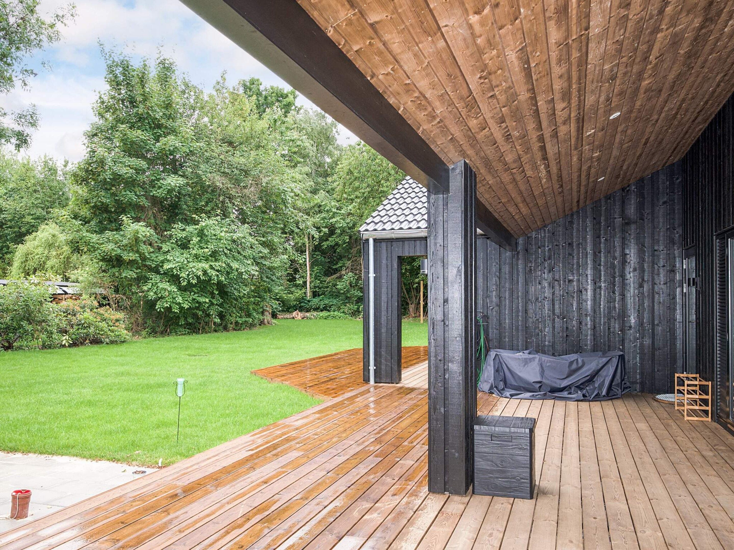 A wooden deck with a covered area, surrounded by a lush green lawn and trees.