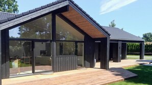 A modern building with large glass windows, a wooden deck, and a covered outdoor area. - 4 Star Holiday Home in Gilleleje (Gilleleje)