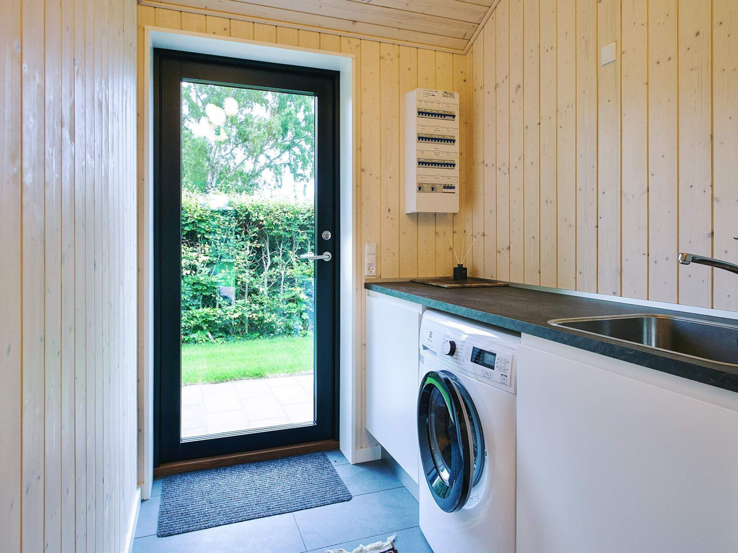 Une buanderie équipée d’un lave-linge, d’un évier et d’un thermostat fixé au mur.