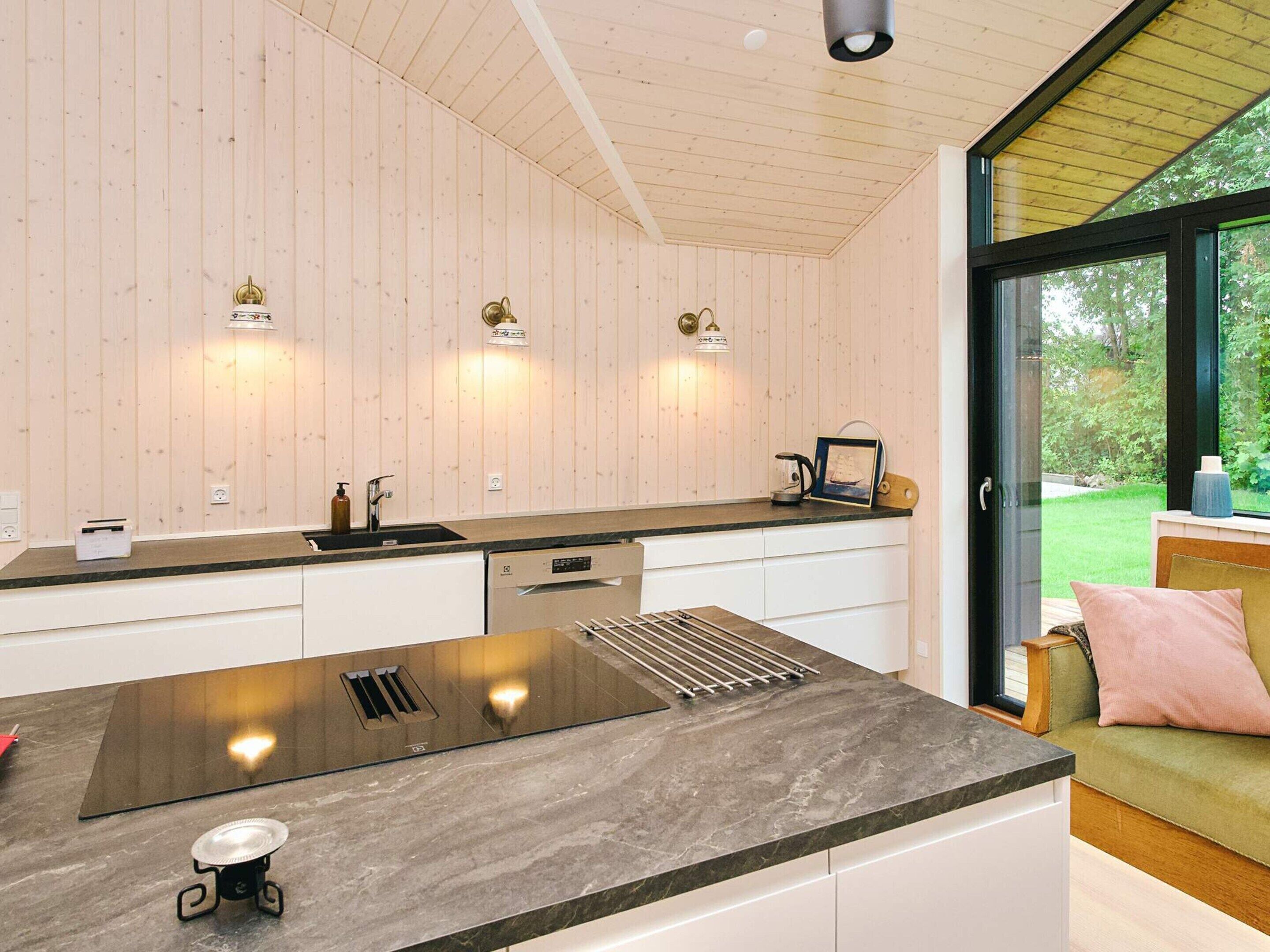A modern kitchen with a large island, wooden walls, and a view of a garden through a glass door.