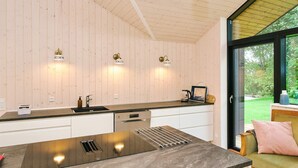 A modern kitchen with a large island, wooden walls, and a view of a garden through a glass door. - 4 Star Holiday Home in Gilleleje (Gilleleje)
