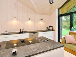 A modern kitchen with a large island, wooden walls, and a view of a garden through a glass door. - 4 Star Holiday Home in Gilleleje (Gilleleje)