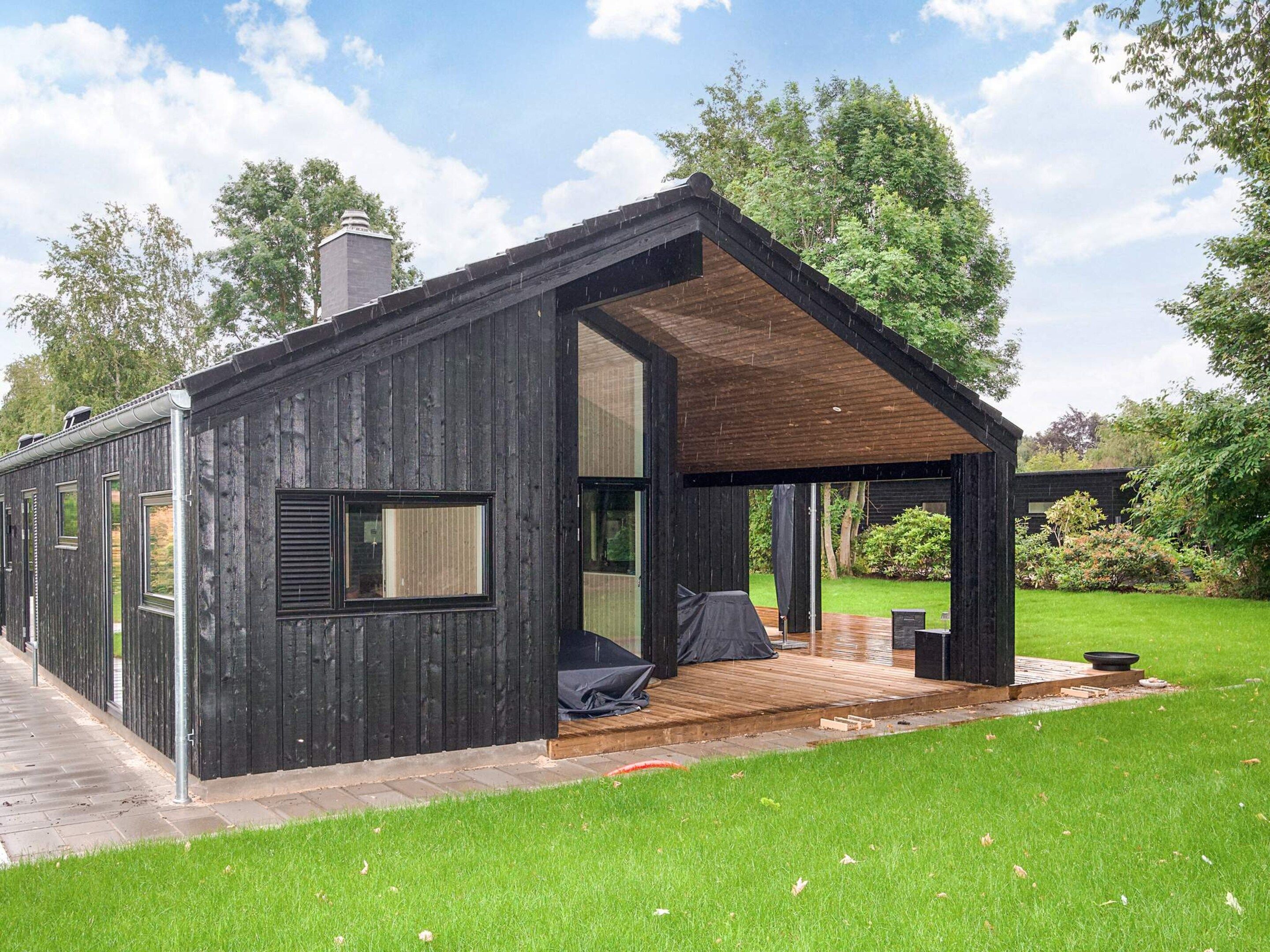 A modern wooden cabin with a covered porch, a chimney, and a grassy yard.
