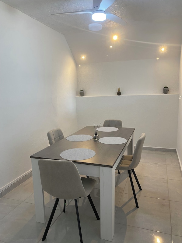 Un comedor con una mesa rectangular, cuatro sillas y un ventilador de techo.