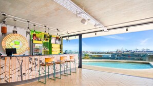 A modern bar with a pool view, featuring a unique circular sign, bar stools, and a green shelving unit.