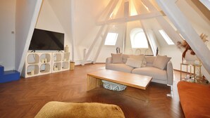 Ein geräumiges Schlafzimmer im Loft-Stil mit großem Fenster, einem Bett, einem Schreibtisch und einem Sessel.