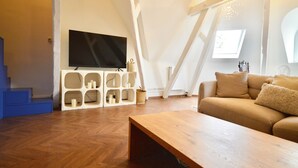 Ein modernes Wohnzimmer mit Holzboden, einem beigen Sofa, einem Holztisch, einem an einer weißen Wand montierten Fernseher und einer einzigartigen weißen Regaleinrichtung mit mehreren Fächern.