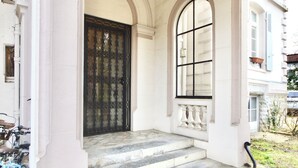 Ein Gebäudeeingang mit einem großen Bogenfenster, einem schwarzen Tor und Stufen, die zur Tür führen.